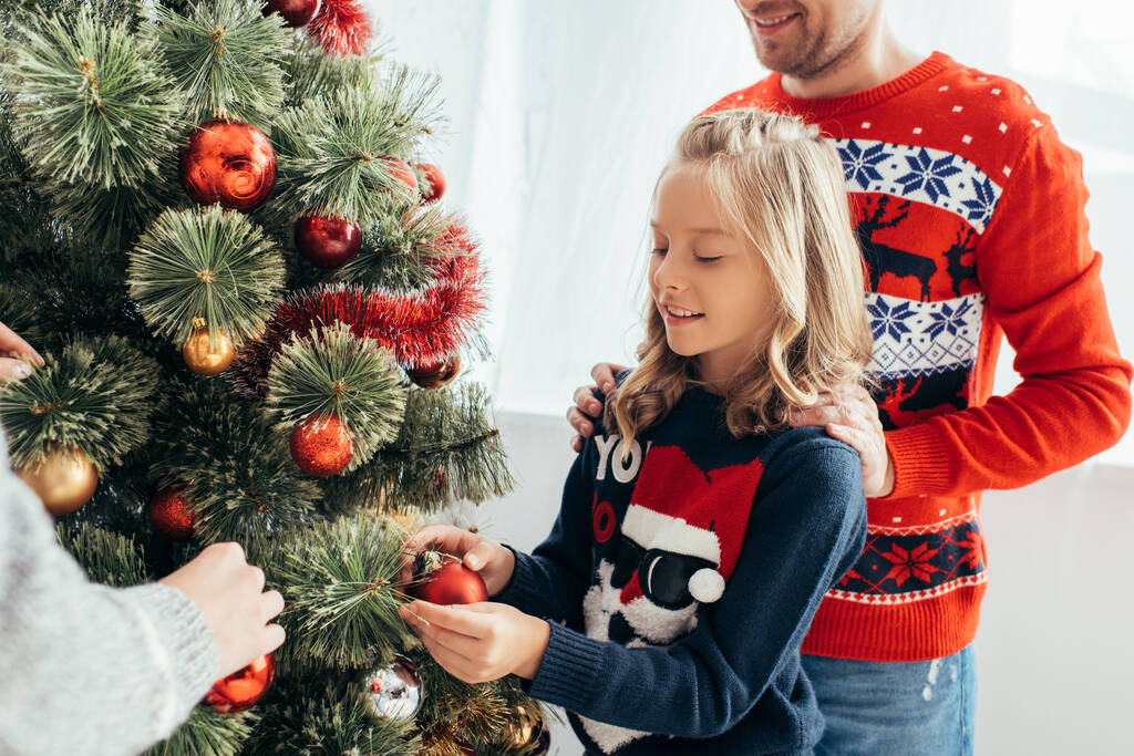 gelukkig kind versieren kerstboom met ouders thuis  - Foto, afbeelding