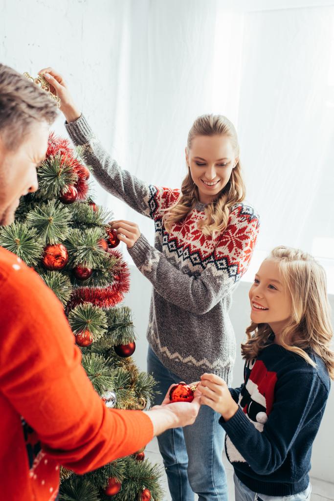 niño feliz decorando el árbol de Navidad con padres alegres en casa  - Foto, Imagen