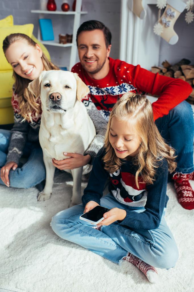 radostné dítě pomocí smartphonu s prázdnou obrazovkou v blízkosti rodičů a psa doma - Fotografie, Obrázek
