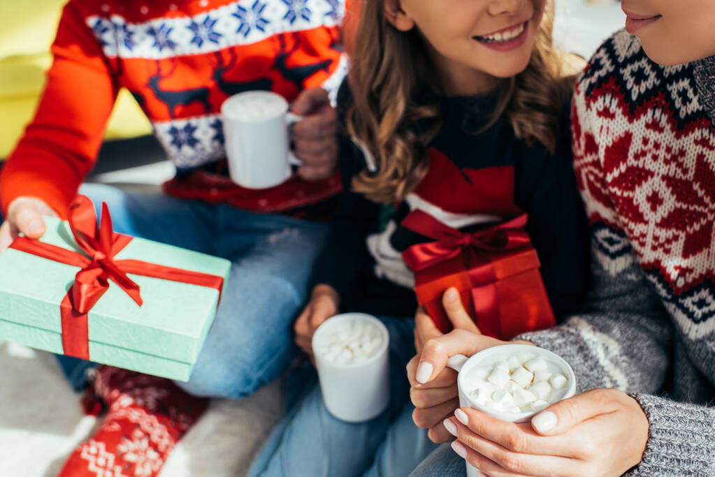 przycięty widok rodziny w swetrach trzymając kubki z napojami w pobliżu prezentów na Boże Narodzenie  - Zdjęcie, obraz