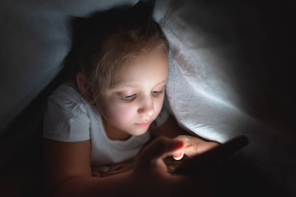 カバーの下にスマートフォンで夜の女の子。小児用ガジェット中毒と不眠症 - 写真・画像