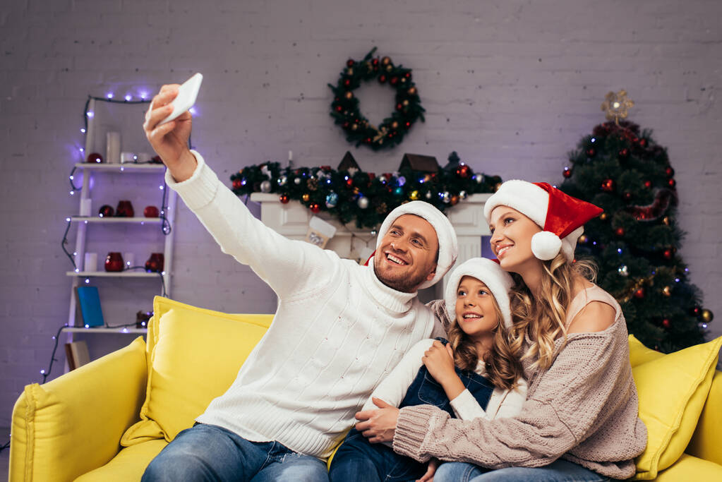 familia feliz en sombreros de santa tomar selfie en sala de estar decorada  - Foto, imagen
