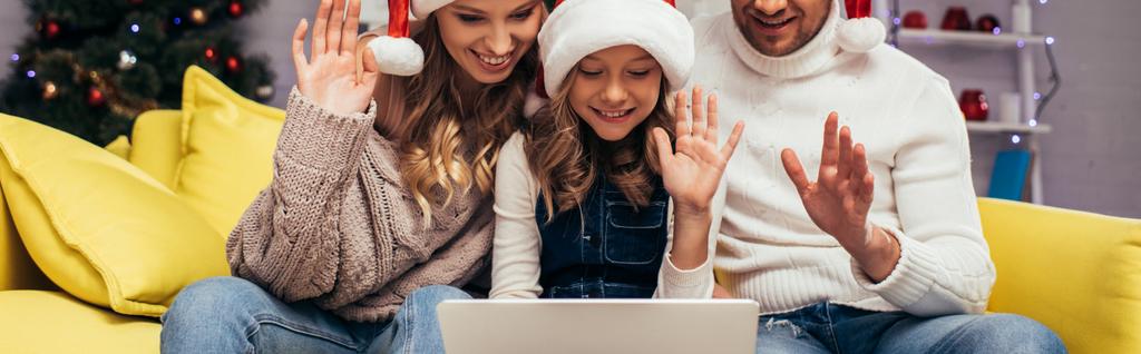 familia alegre en los sombreros de santa saludando las manos mientras que tiene chat de vídeo en Navidad, bandera - Foto, Imagen