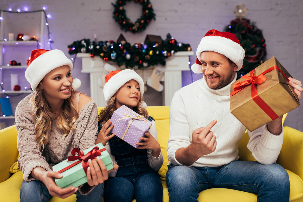szczęśliwa rodzina w Santa kapelusze gospodarstwa prezenty w urządzonym salonie na Boże Narodzenie  - Zdjęcie, obraz