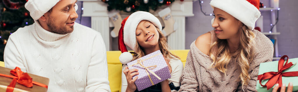 famiglia gioiosa in cappelli di Babbo Natale che tiene regali in soggiorno decorato a Natale, banner - Foto, immagini