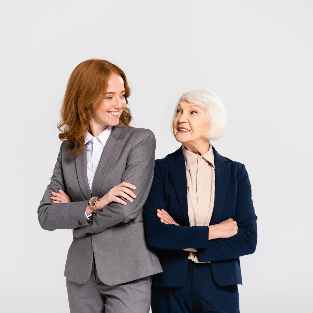 Mujeres de negocios sonrientes con los brazos cruzados mirándose aisladas en gris - Foto, Imagen