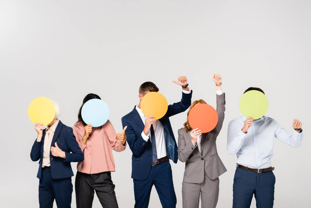 Мультикультурные предприниматели, показывая как жест, закрывая лица карточками, изолированными на сером - Фото, изображение