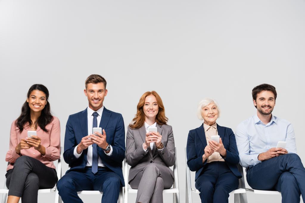 Lächelnde multikulturelle Geschäftsleute mit Smartphones isoliert auf grau - Foto, Bild