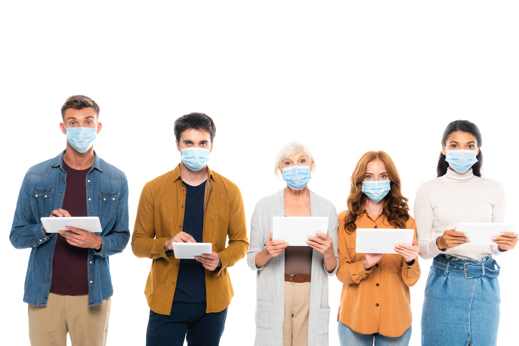 Мультикультурные люди в медицинских масках и с использованием цифровых таблеток, изолированных на белом - Фото, изображение