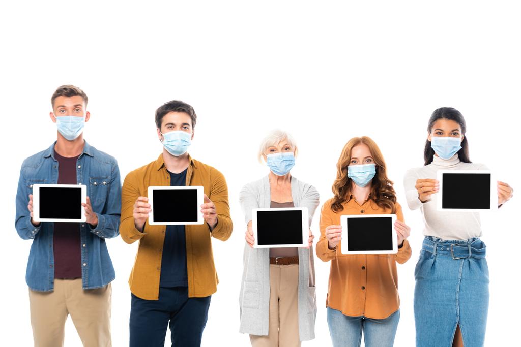 Wieloetniczni przyjaciele w maskach medycznych pokazujący cyfrowe tabletki z pustym ekranem odizolowanym na biało - Zdjęcie, obraz