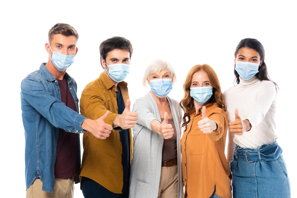 Amigos multiculturales mostrando como mientras usan máscaras médicas aisladas en blanco - Foto, imagen