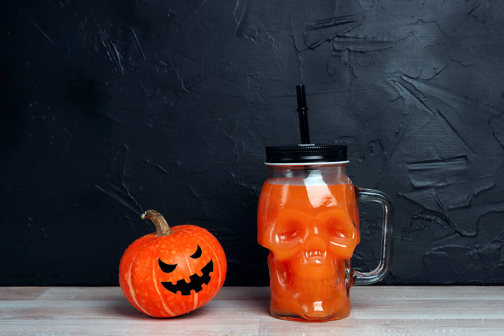 Orangefarbener Halloween-Cocktail im Totenkopf-Glas mit Kürbiskopf-Jack-Laterne auf schwarzem Hintergrund. Kopierraum für Text. - Foto, Bild