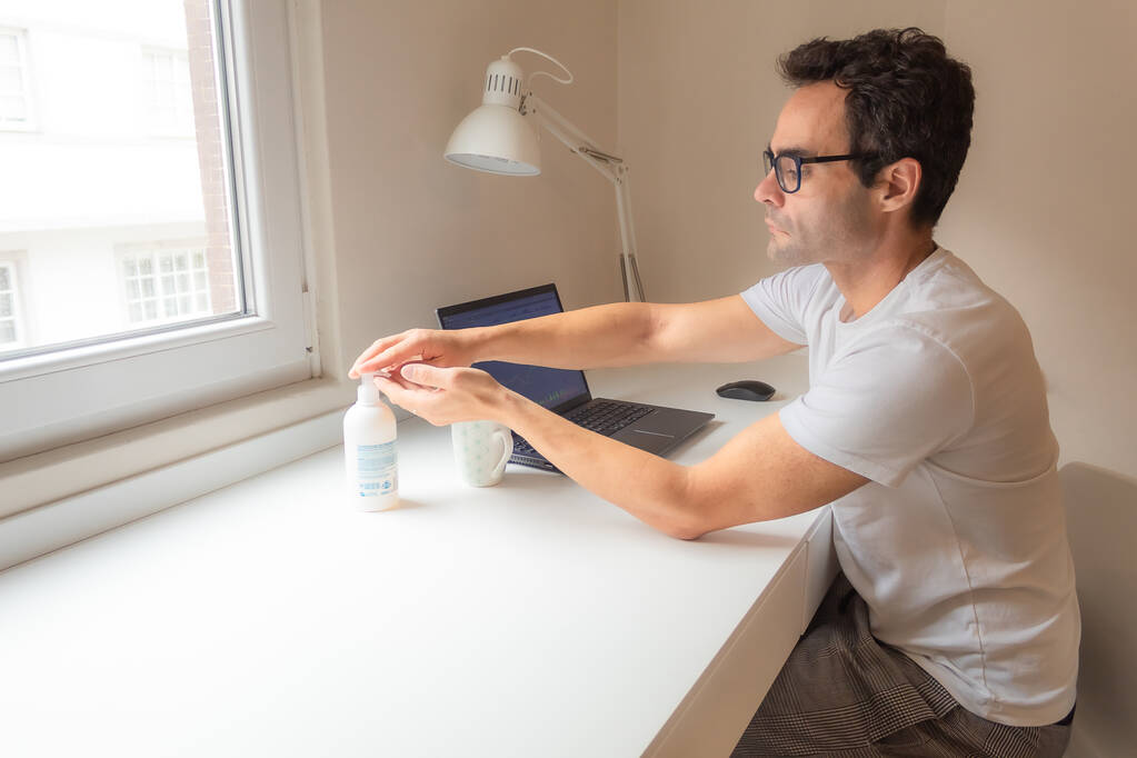 Mladý podnikatel používající dezinfekci rukou při práci doma během pandemie - Fotografie, Obrázek