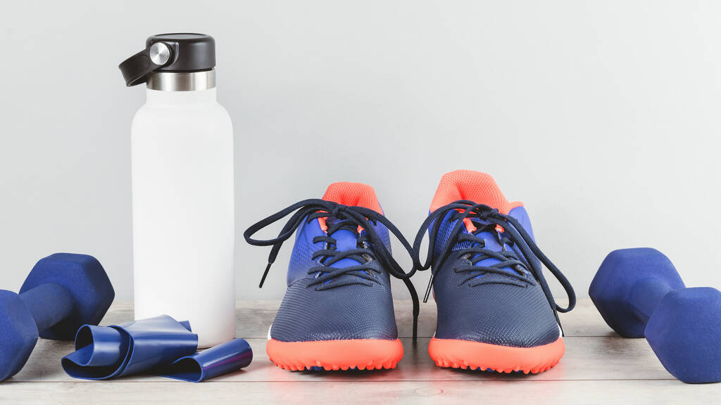 Sağlıklı yaşam tarzı mavi ve kırmızı cinsiyetli tarafsız spor aksesuarları beyaz ahşap üzerinde beyaz su şişesi şişesiyle gruplandırılmış. Fitness ve ev ya da spor egzersizi monokrom unsurlar afişi kopya alanı - Fotoğraf, Görsel