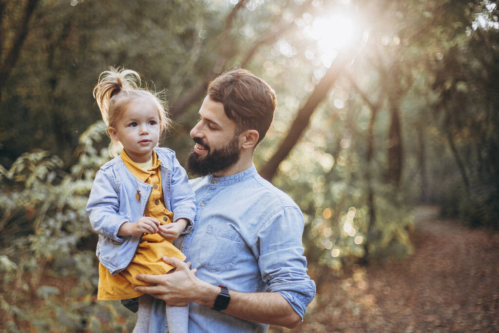 молодой, стильный бородатый отец гуляет со своей маленькой дочерью на природе на закате. Семейные фотографии отца и одного ребенка. селективная фокусировка, эффект шума - Фото, изображение