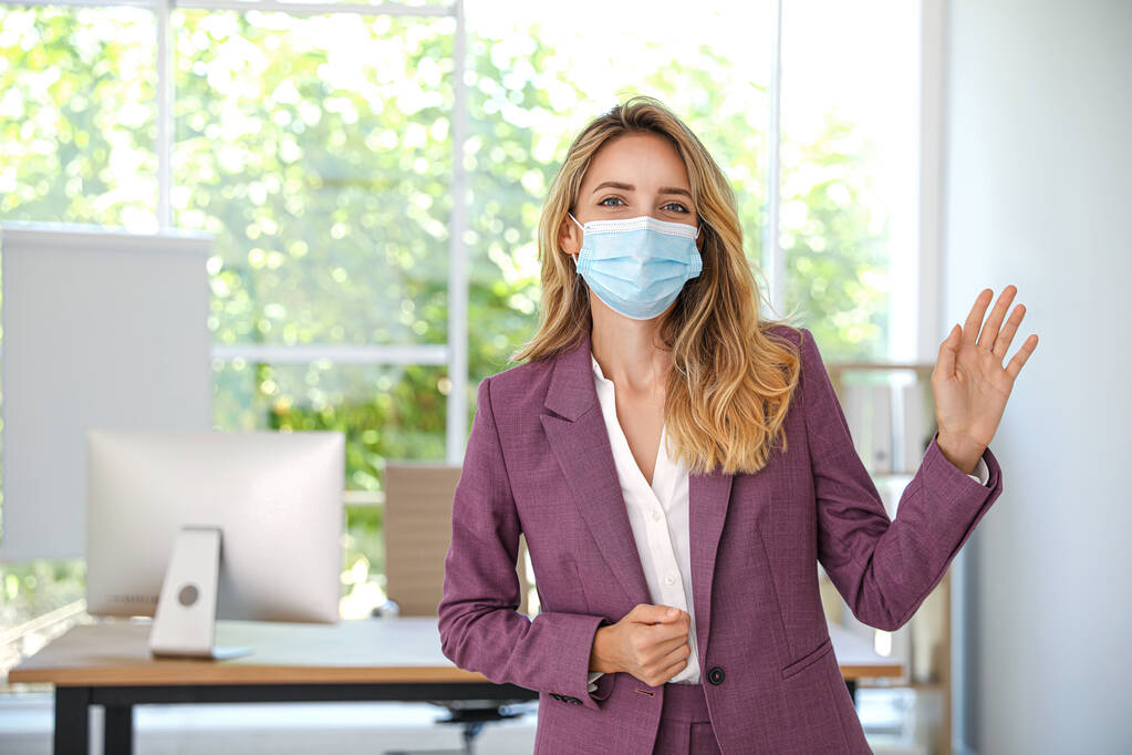 Frau in Schutzmaske mit Hallo-Geste im Amt. Soziale Distanz bei Coronavirus-Pandemie wahren - Foto, Bild