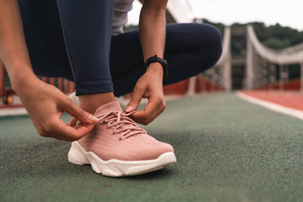 Primo piano della giovane donna che si prepara per fare jogging all'aperto allacciandosi le scarpe da ginnastica rosa. Concetto di salute e sport - Foto, immagini