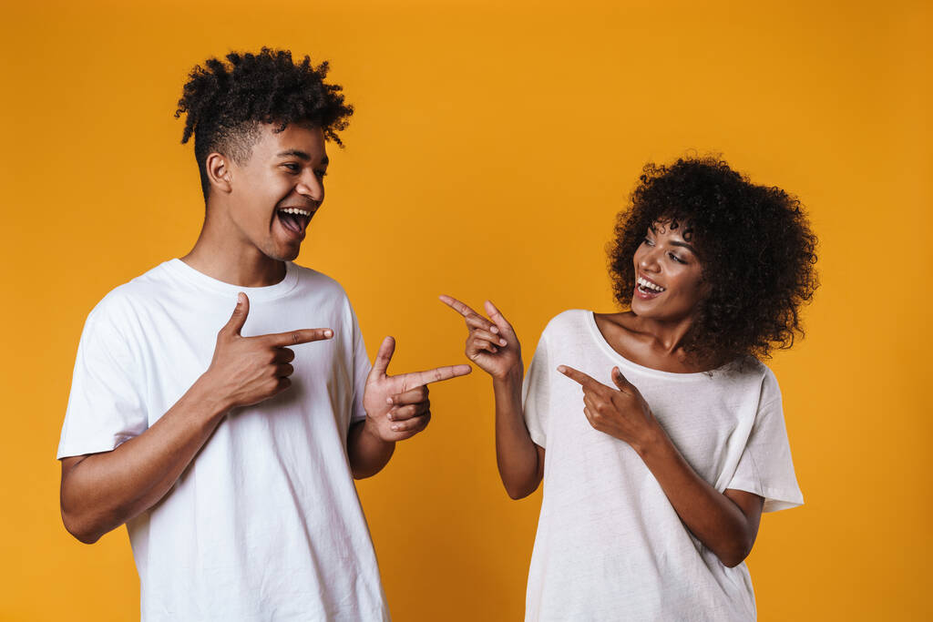 Image d'un couple afro-américain joyeux pointant du doigt l'un l'autre isolé sur un mur jaune - Photo, image