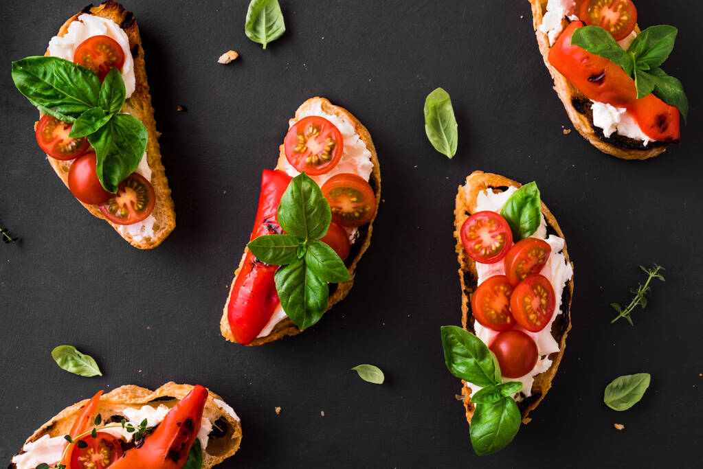 Bruschetta sandwiches met tomaten, roomkaas, gegrilde paprika en basilicum op donkere achtergrond, bovenaanzicht, kopieerruimte. Traditionele Italiaanse snack - gegrilde bruschetta toastjes. - Foto, afbeelding