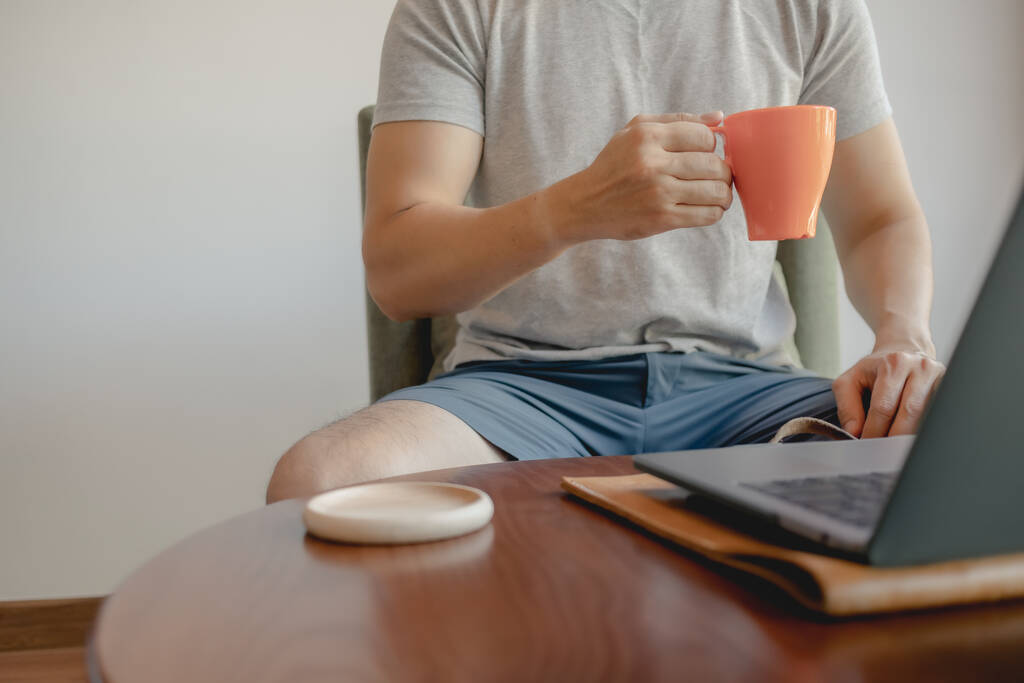 Чоловік бере чашку кави, працюючи на своєму ноутбуку.. - Фото, зображення