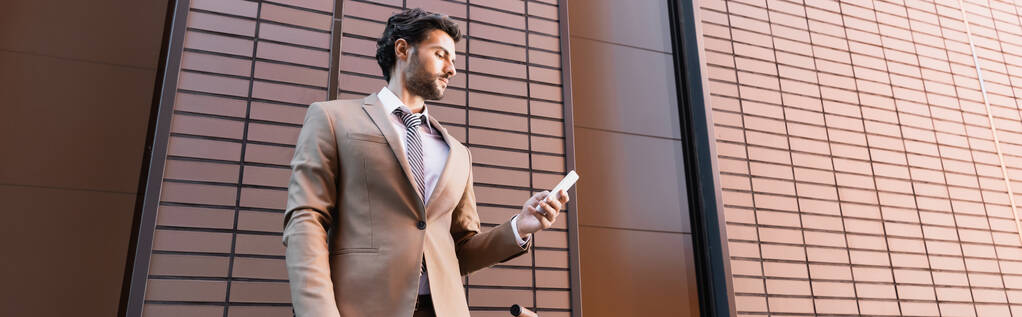 parrakas liikemies katselee älypuhelinta rakennuksen lähellä, banneri - Valokuva, kuva