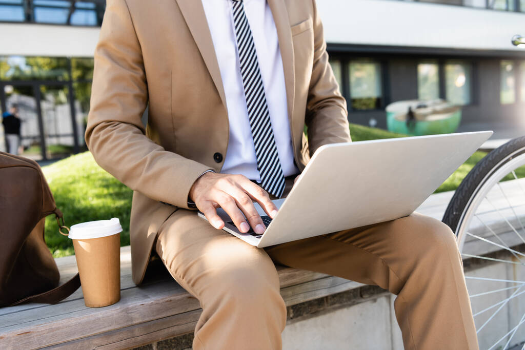 rajattu näkymä liikemies kannettavan tietokoneen lähellä paperimuki - Valokuva, kuva