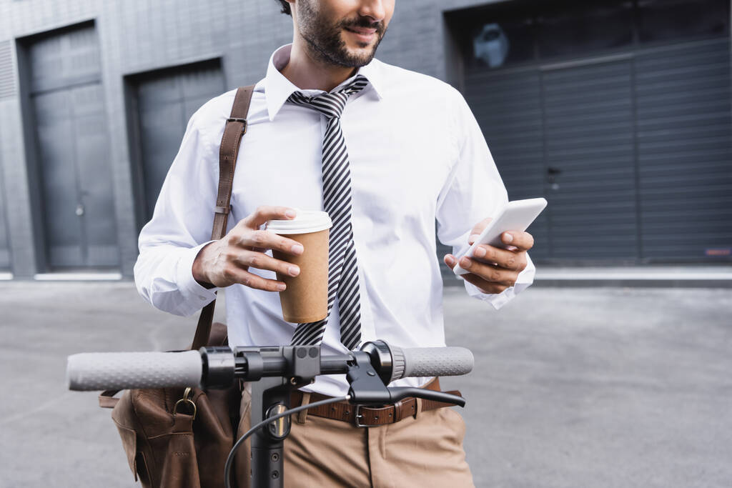 rajattu näkymä parrakas liikemies muodollinen kulumista tilalla paperi cup ja älypuhelimella lähellä e-skootteri  - Valokuva, kuva