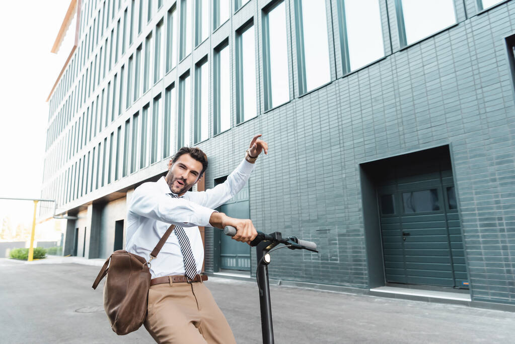 excitado hombre de negocios en el desgaste formal montar scooter eléctrico cerca del edificio  - Foto, imagen
