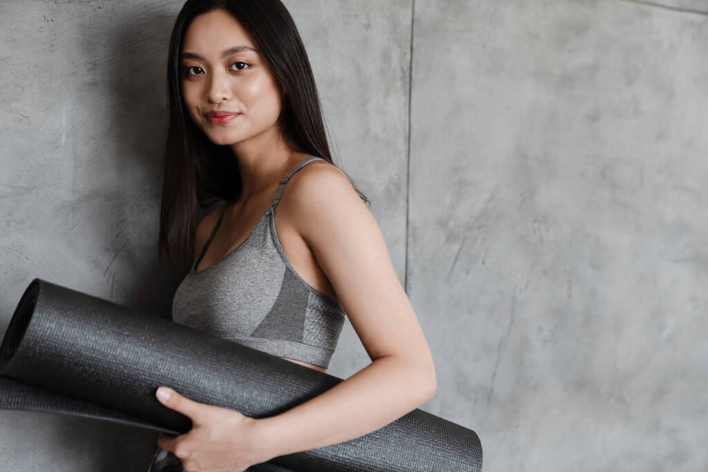 Bild der schönen asiatischen Mädchen in Sportbekleidung posiert mit Yogamatte zu Hause - Foto, Bild
