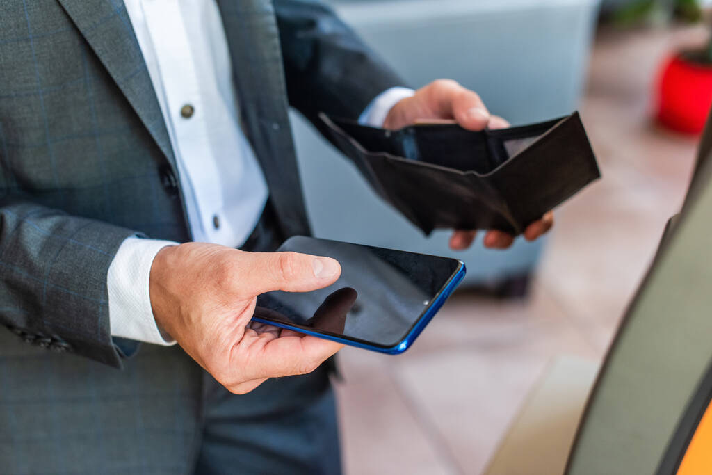 Cropped view of businessman holding empty wallet and smartphone with blurred street on background - Photo, Image