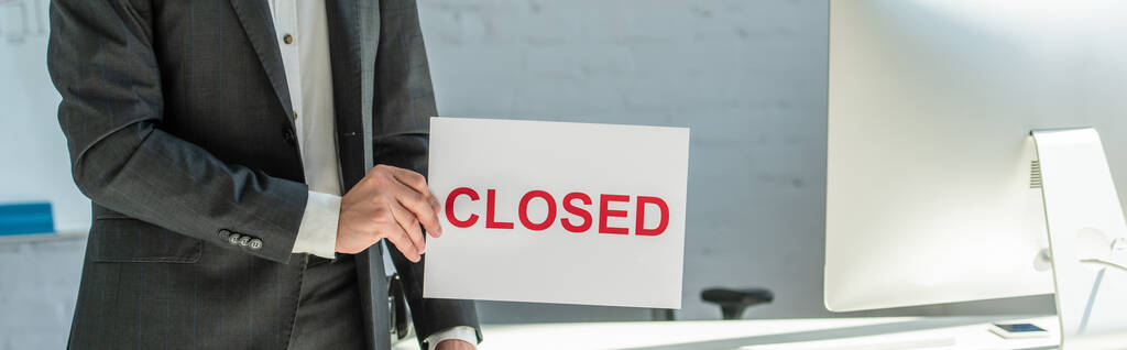 Cropped view of businessman holding sign with closed lettering, while standing near workplace on blurred background, banner - Photo, Image
