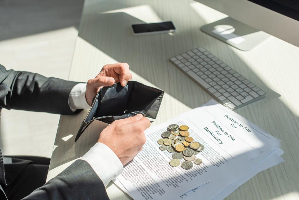 Ausgeschnittene Ansicht eines Geschäftsmannes mit leerem Portemonnaie in der Nähe von Münzen und Insolvenzanträgen am Arbeitsplatz - Foto, Bild