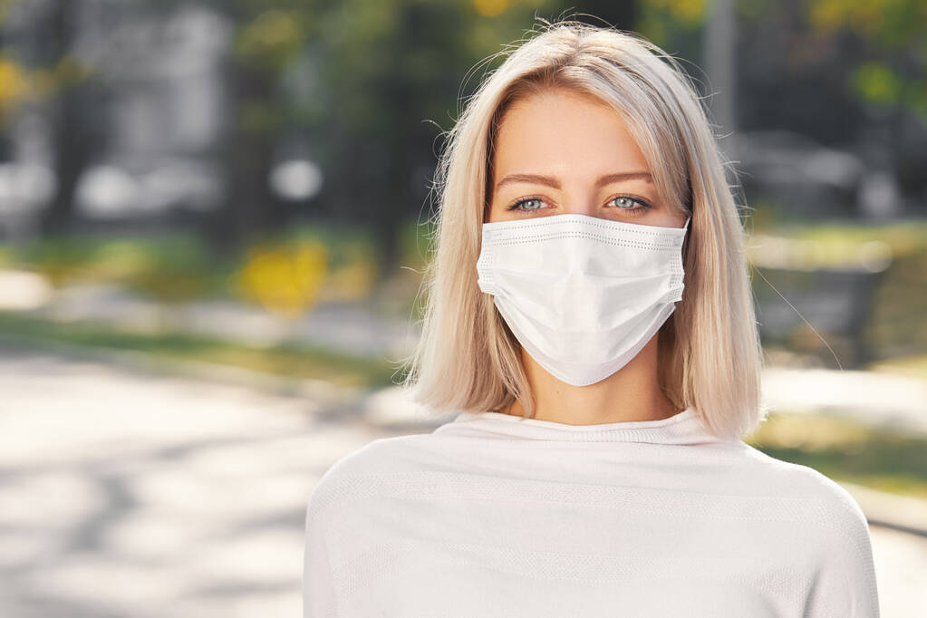 Nuori nainen yllään suojaava lääketieteellinen naamio ulkona aurinkoisena päivänä pandemian aikana coronaviru - Valokuva, kuva