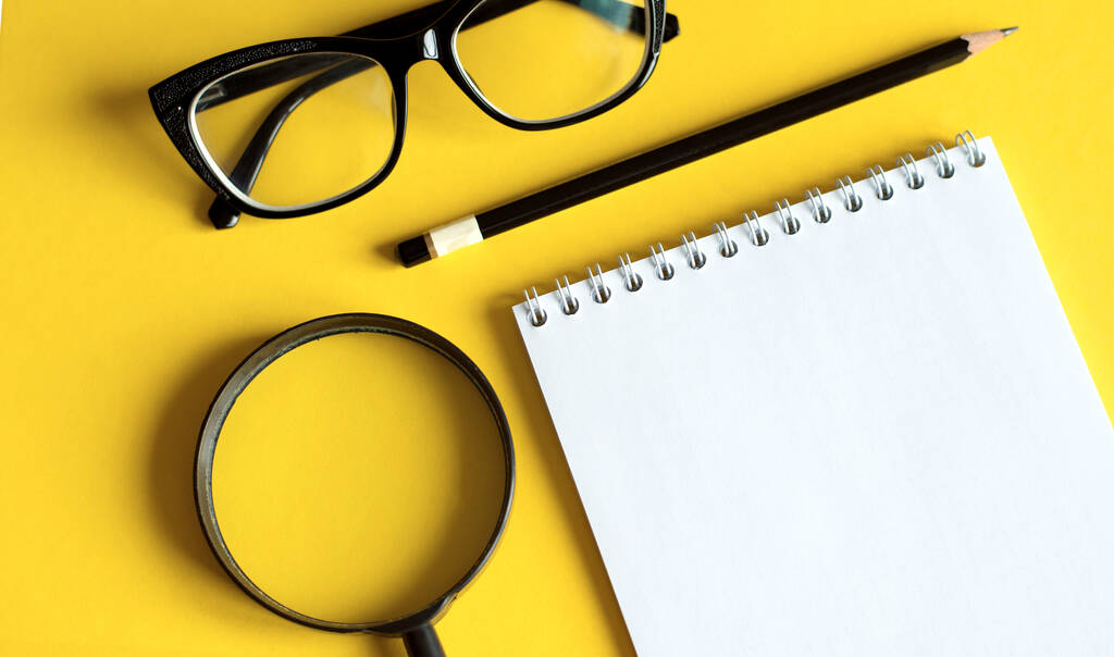 黄色の背景にノート、拡大鏡、黒眼鏡でビジネスコンセプト - 写真・画像