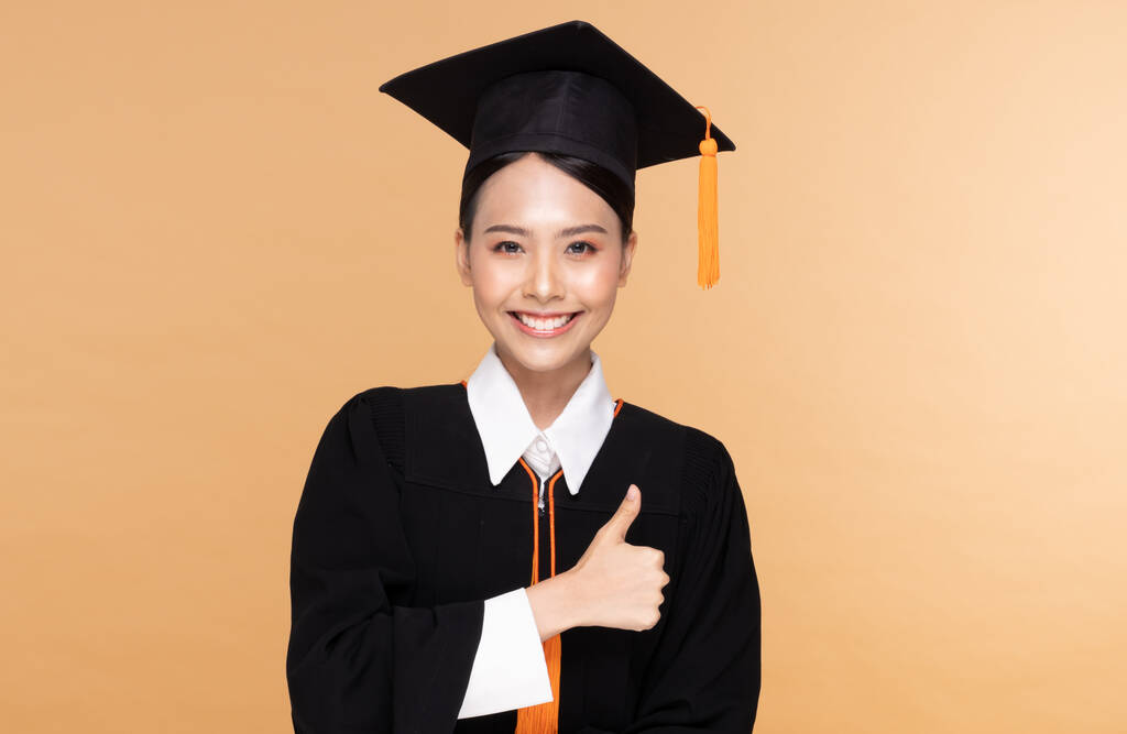 Hermosa mujer asiática atractiva graduada en gorra y vestido sonrisa tan orgullosa y felicidad, aislada en fondo beige, concepto de éxito educativo - Foto, imagen
