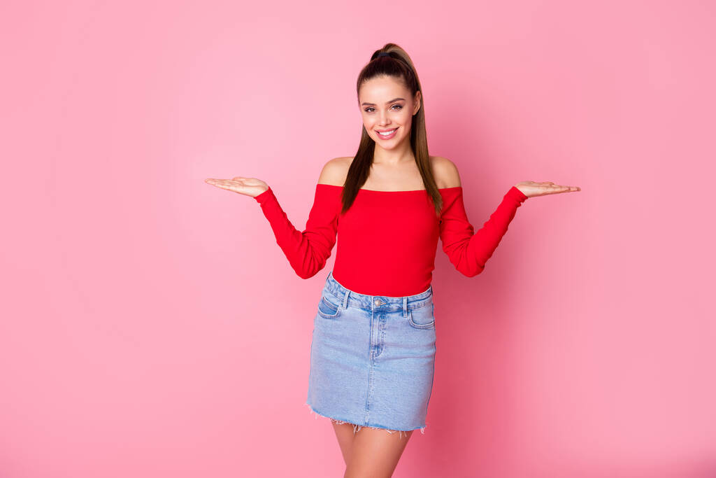 Photo of attractive lady hold open arms empty space advising pick one of two best products wear casual red open shoulders shirt mini denim skirt isolated pastel pink color background - Photo, Image