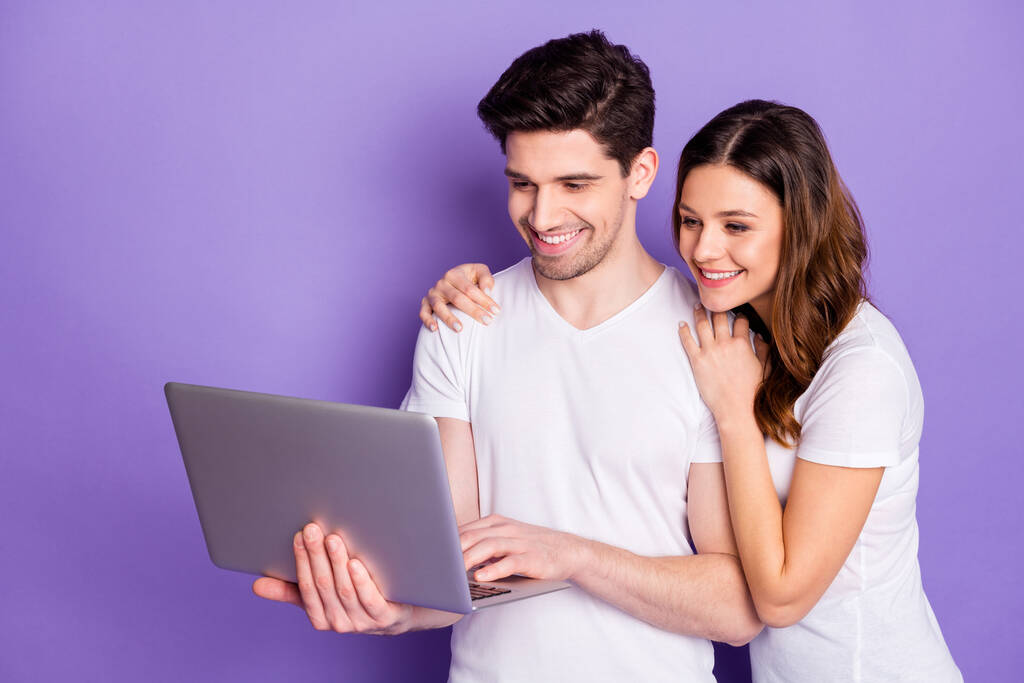 Photo pretty lady handsome guy married couple good mood hold notebook hands watch movie film together speak skype relatives wear casual white t-shirts isolated purple color background - Photo, Image