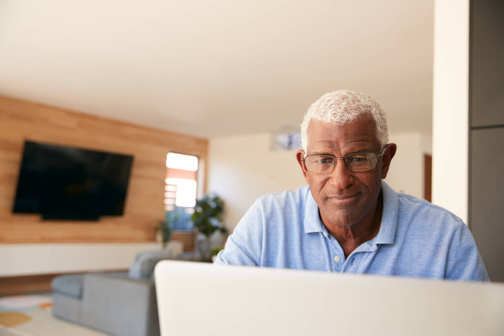 Старший афроамериканец использует ноутбук, чтобы проверить финансы дома - Фото, изображение