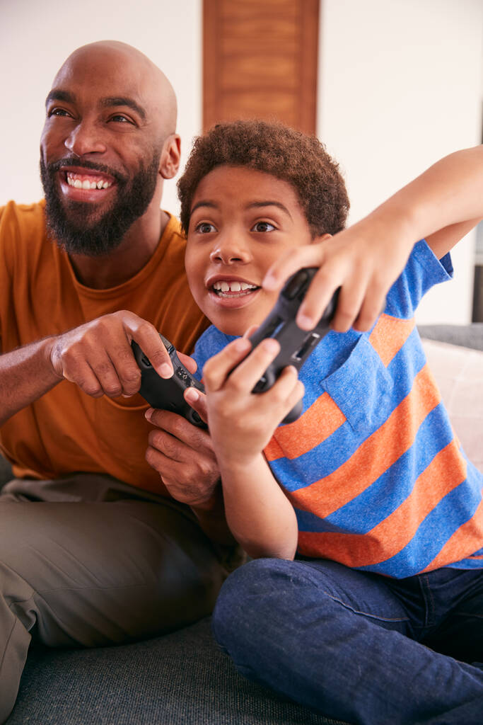 アフリカ系アメリカ人の父と息子が自宅でソファに座ってビデオゲームを一緒にプレイ - 写真・画像