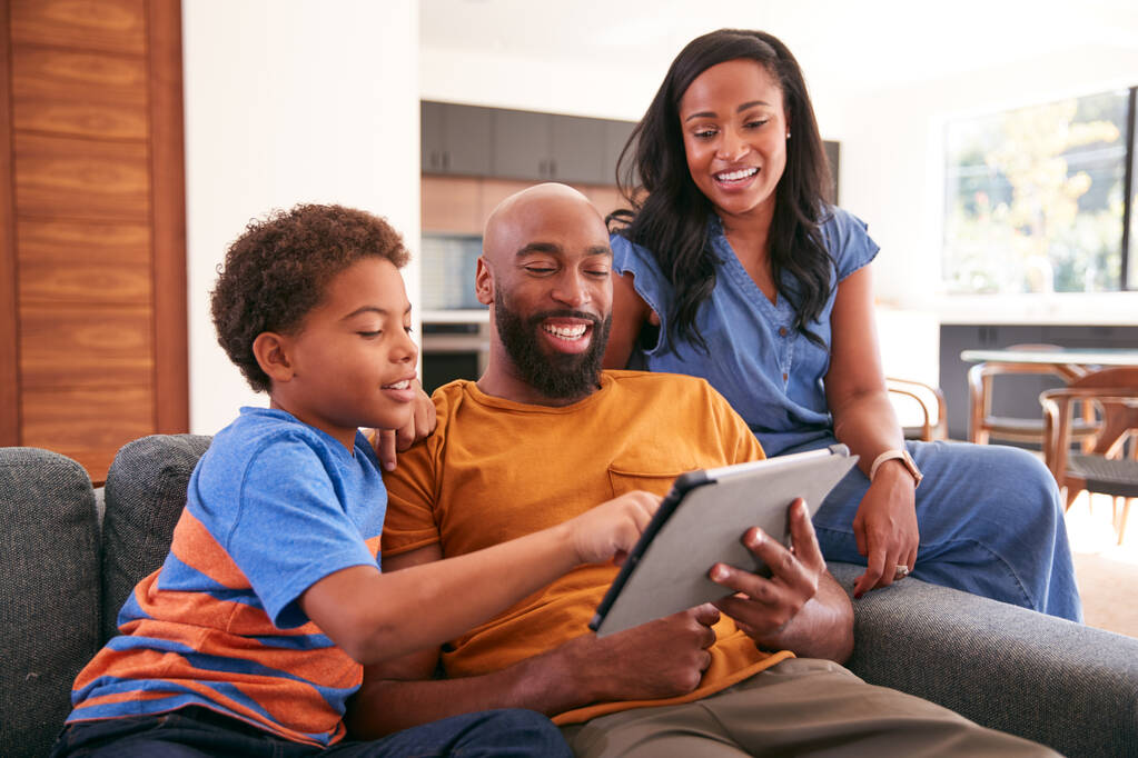 Афроамериканская семья с сыном сидит на диване дома с помощью цифрового планшета - Фото, изображение