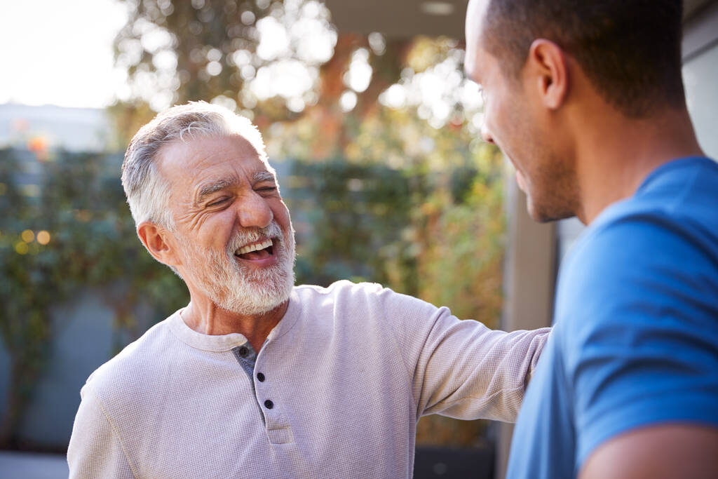 Hombre hispano mayor hablando y riendo con hijo adulto en el jardín en casa - Foto, imagen