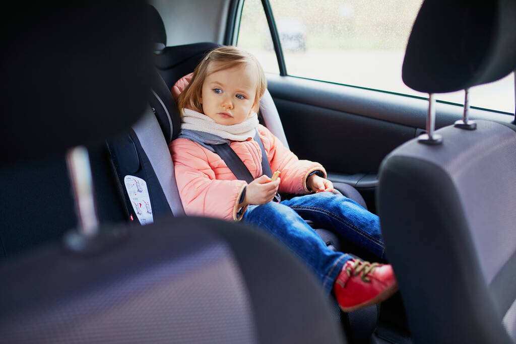 Adorable niña en el asiento de coche moderno comer galleta. Un niño viajando en coche. Seguridad infantil en la carretera. Viaje con un bebé - Foto, Imagen