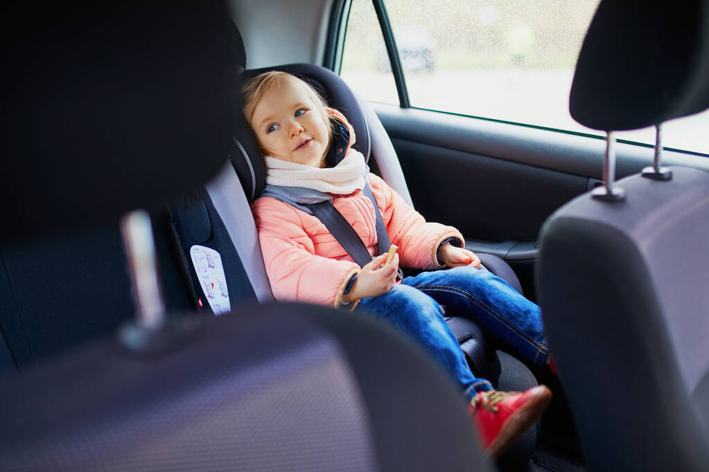 Adorable niña en el asiento de coche moderno comer galleta. Un niño viajando en coche. Seguridad infantil en la carretera. Viaje con un bebé - Foto, imagen