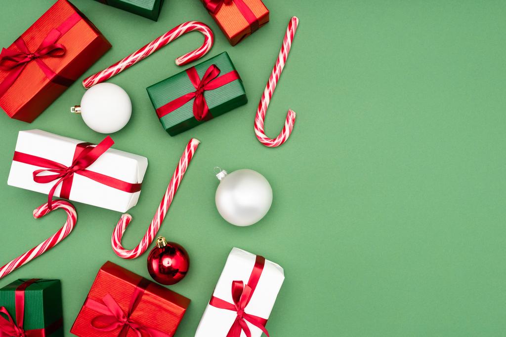 Ansicht von bunten Geschenkboxen, Zuckerstangen und Weihnachtskugeln auf grünem Hintergrund - Foto, Bild