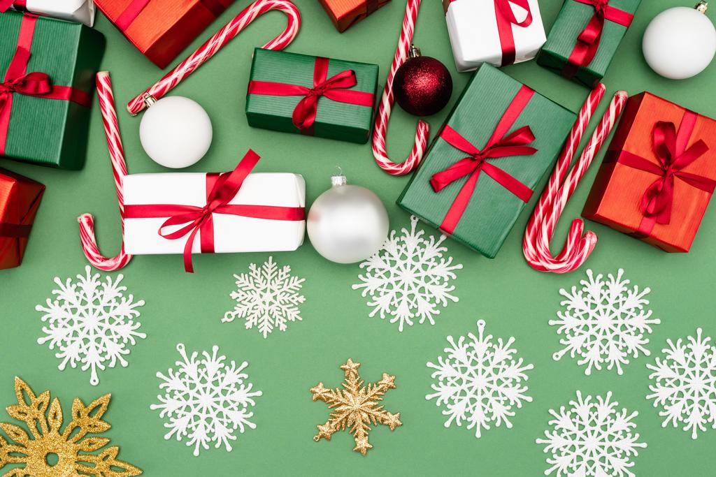 vrchní pohled na pestrobarevné dárkové krabice, candy canes, vánoční koule a dekorativní sněhové vločky na zeleném pozadí - Fotografie, Obrázek