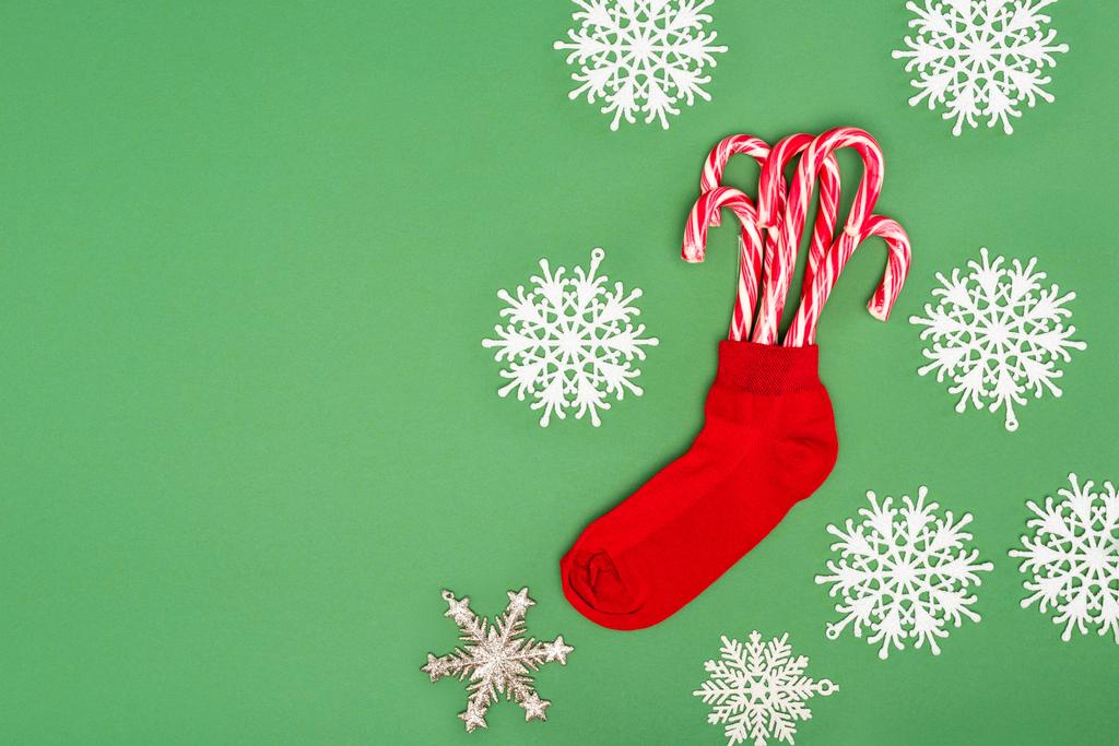 bas de Noël rouge avec des cannes de bonbons près de flocons de neige décoratifs sur vert - Photo, image