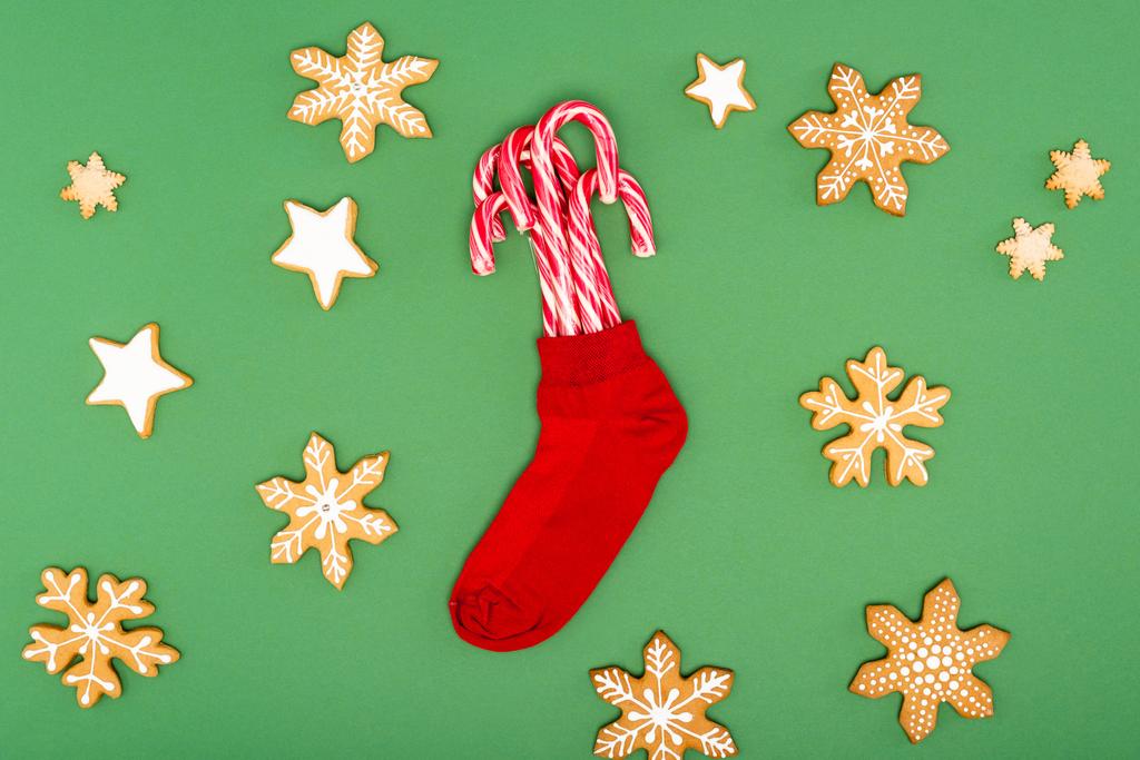 κορυφή άποψη του κόκκινου χριστουγεννιάτικη κάλτσα με καραμέλα μπαστούνια κοντά υποστηρίζεται αστέρια και νιφάδες χιονιού σε πράσινο φόντο - Φωτογραφία, εικόνα
