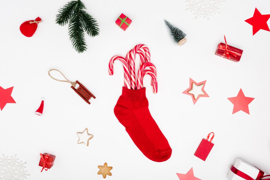calza di Natale rosso con bastoncini di zucchero vicino ai biscotti e bagattelle festive su sfondo bianco - Foto, immagini