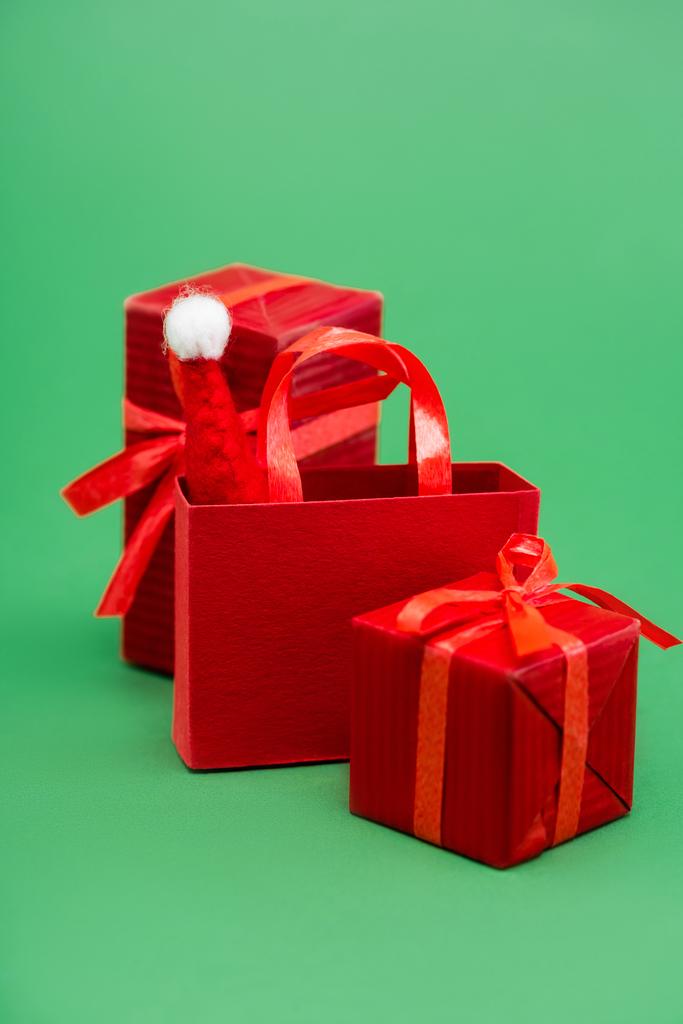 rode geschenkdozen en boodschappentas met kerstmuts op groene achtergrond - Foto, afbeelding
