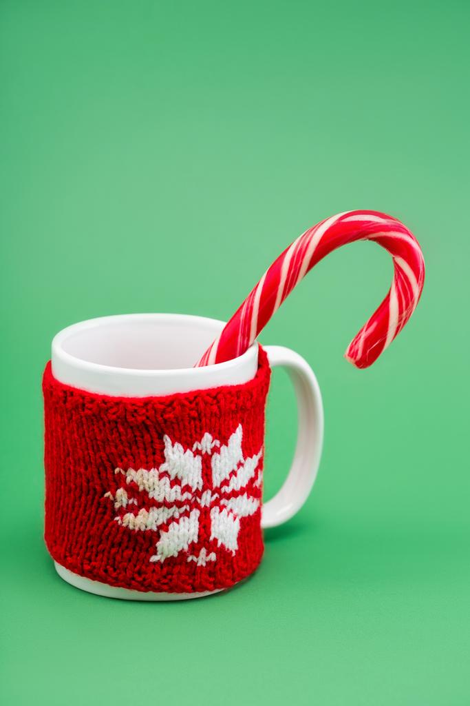 цукеркова тростина в чашці з в'язаним тримачем чашки зі сніжинкою на зеленому фоні
 - Фото, зображення